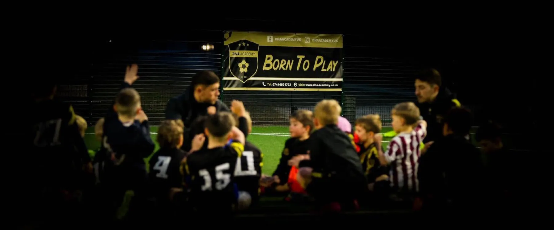 Young DNA Academy players gathered around a coach in front of the Born to Play banner