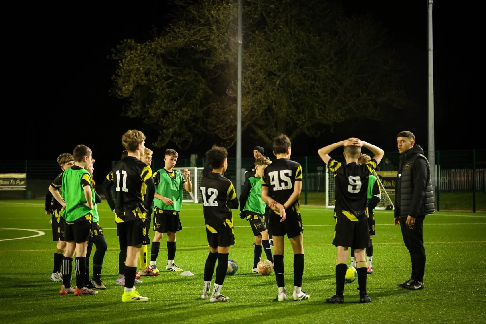 A DNA Academy coach leading a team talk under floodlights